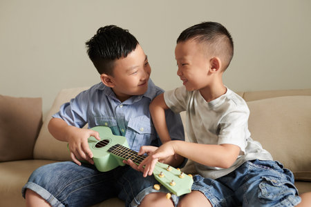 Cheerful preteen boy asking brother to let him play ukulele