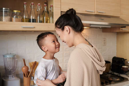Happy young mother talking to little son sitting on kitchen counterの写真素材