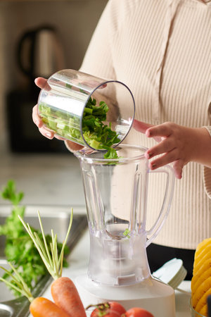 Close-up image of woman putting bowl of cut celery in blender