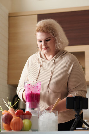 Curvy young woman filming herself making red dragonfruit smoothie for brealfastの写真素材