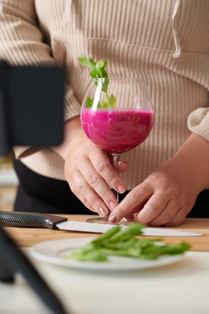 Hands of woman putting glass of delicious red smoothie with arugula she made for breakfast on table...