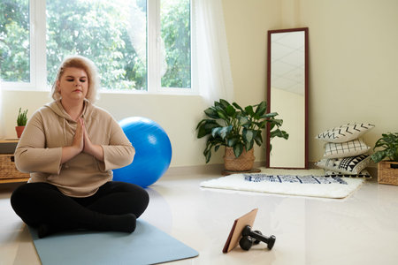 Plus-size young woman following lesson on tablet computer when practicing yoga at home
