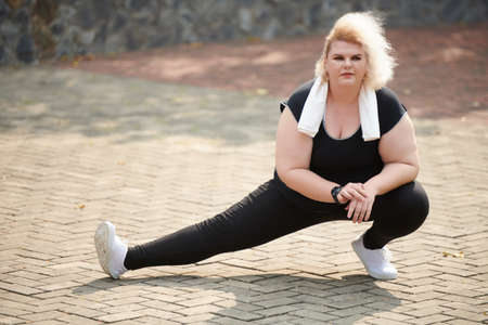 Flexible young curvy sportswoman doing side lunges to stretch legs after runの写真素材