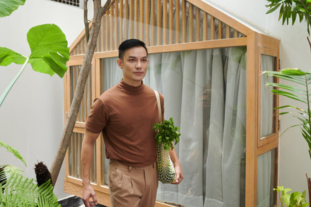 Smiling young Asian with reusable bag walking home after shopping at local marketの写真素材