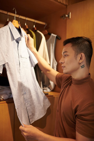 Young man standing in closet and holding hanger with choosing to wear organic cotton shirt for today