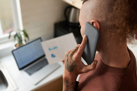 Young man checking report with charts and diagrams and talking on phone with colleague