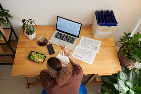 UI designr eating lunch at desk in his home office when working on wireframe of interface designの写真素材