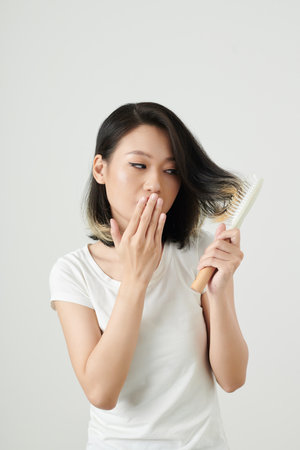 Young Asian woman covering mouth when looking at brush stuck in hairの写真素材