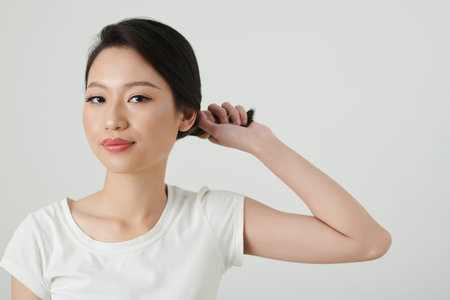 Portrait of smiling young woman twisting hair when making elegant bunの写真素材