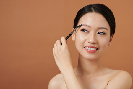 Lovely smiling young woman brushing up eyebrows to add textureの写真素材