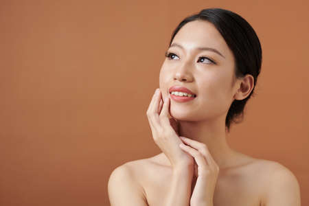 Smiling young woman touching tender skin of her face and looking upの写真素材