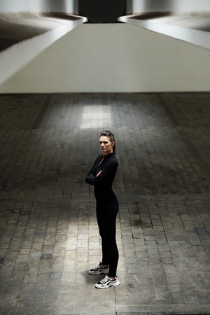 Confident determined sportswoman crossing arms and looking at camera when standing in underground...