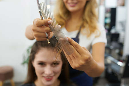 Process of hairdresser cutting hair of smiling young woman in beauty salonの写真素材