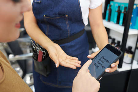 Hairdresser asking client to leave feedback via mobile application after getting hair done in beauty salonの写真素材