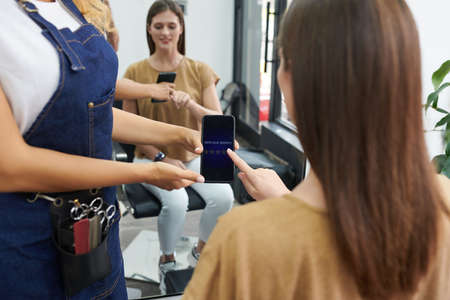 Hairdresser asking client to rate service of beauty salon via application on smartphoneの写真素材