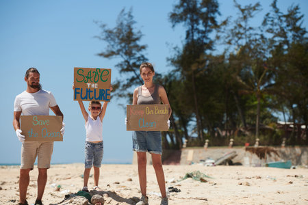 Happy family with handmade placards standing on dirty beach and asking to save the ocean