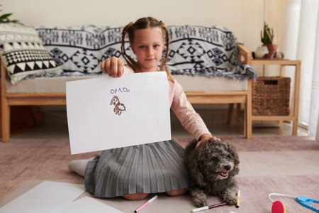 Little girl showing drawing of dog when sitting on floor at home next to herの写真素材