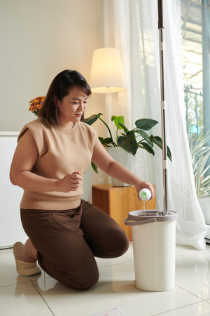 Woman adding cleaning and disinfecting detergent in mop bucket with water