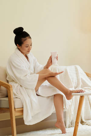 Young Asian woman applying body lotion to moisturize skin after showerの写真素材