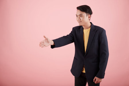 Smiling young Asian entrepreneur outstretching arm for handshake for greeting business partner