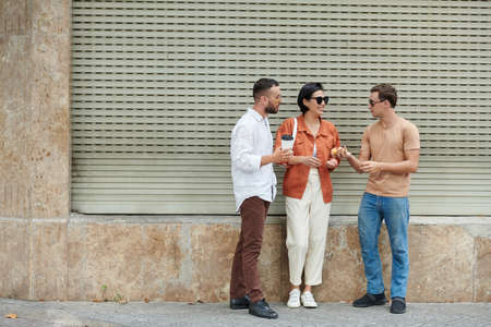 Young man giving fresh buns he baked to friends when they are standing against wallの写真素材