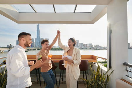 Joyful friends dancing and drinking cocktails in rooftop barの写真素材