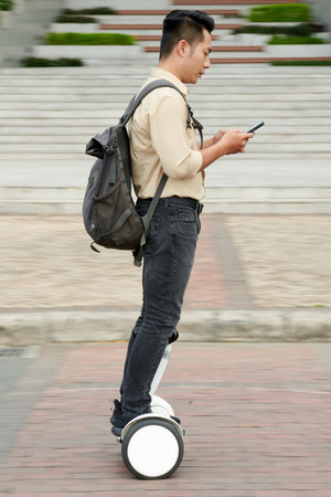 Vietnamese young man checking notifications on smartphone when riding on university campus on...