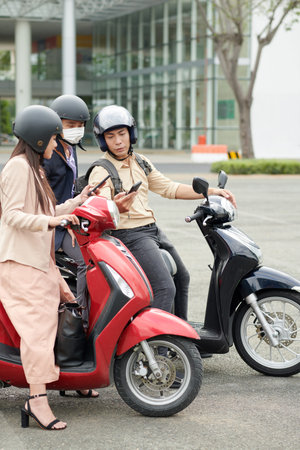 Business colleagues on scooters discussing where to go for lunch break and checking availability on...