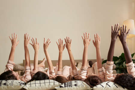 Group of young women lying on floor and raising arms up in the airの写真素材