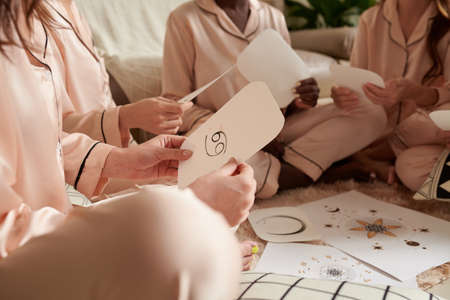 Close-up image of young woman in satin pajama holding card with cancer astrological signの写真素材