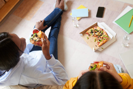 Teenage girls eating pizza after finishing with homework, view from aboveの写真素材