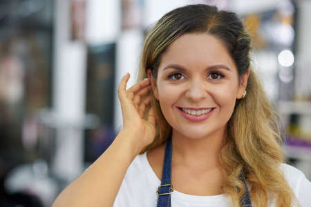 Portrait of smiling young woman working in beauty salon touching her hair and looking at cameraの写真素材