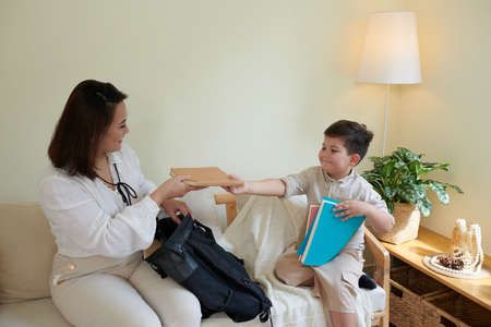 Mother helping little son to pack books for first day of schoolの写真素材