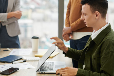 Young business, an with piercing in left ear opening laptop at meeting with colleagues