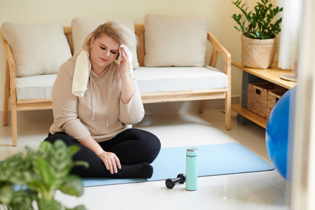 Tired plus size young woman wiping sweat from forehead after finishing daily workout