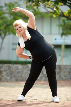 Plus size sportswoman doing side bends when working out outdoors