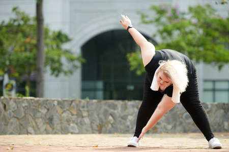 Curvy sportswoman bending forward and stretching hamstrings when working out outdoorsの写真素材