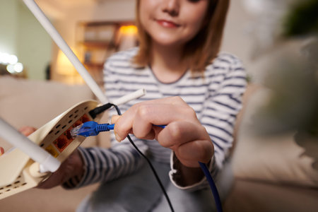 Closeup image of woman plugging Ethernet cord in back of modem to get faster speedの写真素材