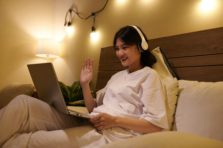 Smiling Vietnamese teenage girl waving with hand when greeting classmates and teacher in online...