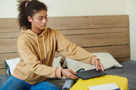 Serious student packing tablet computer in bag when leaving home for universityの写真素材