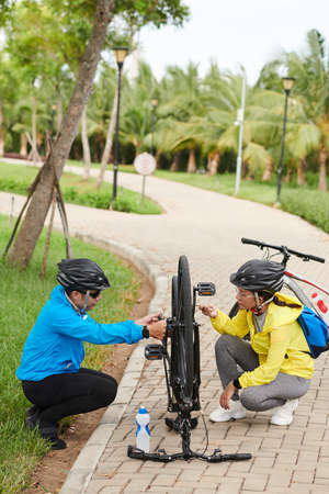 Woman helping boyfriend to fix wheels of bicycleの写真素材