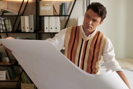 Serious architect looking at big apartment building blueprint in his handsの写真素材