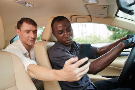 Passenger explaining taxi driver where to ride and showing map on smartphone screenの写真素材