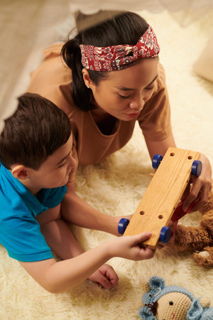Little boy showing mother how to play with wooden toy car