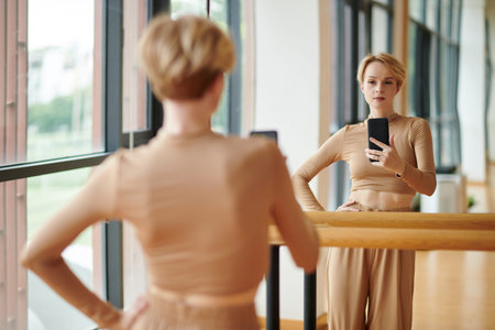 Fit female dancer long sleeve top and wide pants taking selfie in studio mirror