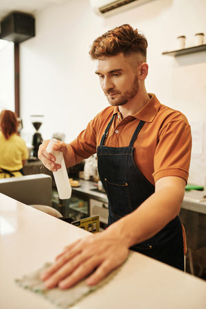 Coffeeshop barista cleaning counter with disinfecting detergent to keep it clean and shiny