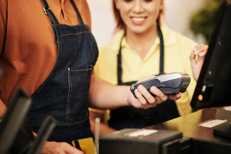 Cafe owner showing new worker how to print receipts after accepting card payment