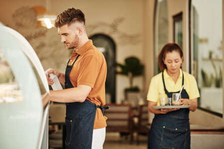 Waiter carrying tray with dirty glasses in kitchen when barista cleaning counter