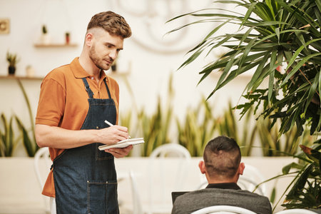 Coffeeshop waiter talking to customer and writing down order details