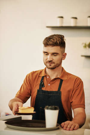 Coffee shop barista putting cup of coffee and piece of cake on trayの写真素材